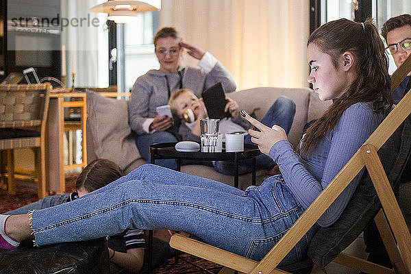 Teenager-Mädchen benutzt Smartphone  während sie sich mit der Familie zu Hause im Wohnzimmer entspannt