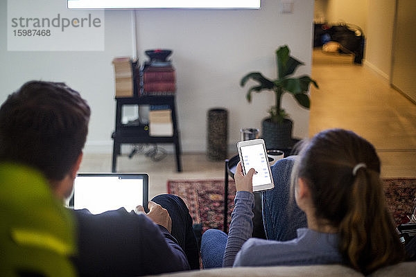 Vater und Tochter nutzen drahtlose Technologien beim Entspannen auf dem Sofa im Smart Home