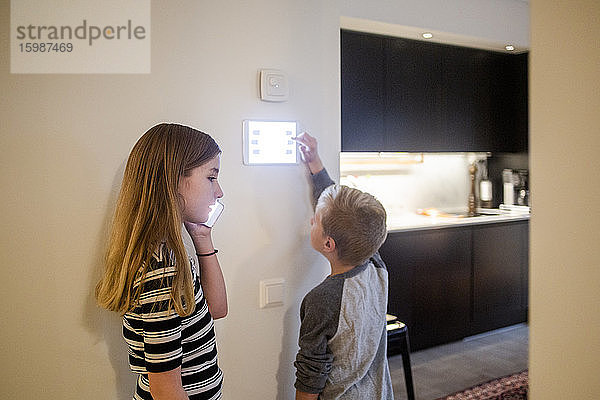 Mädchen telefoniert mit Smartphone  während der Bruder zu Hause ein digitales Tablet an der Wand benutzt