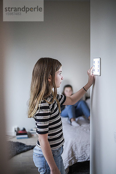 Mädchen mit digitalem Tablett an der Wand mit Schwester im Hintergrund im Smart Home