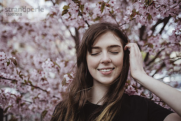 Lächelnde Frau mit geschlossenen Augen an Baum stehend