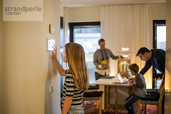 Mädchen benutzt digitales Tablett an der Wand mit Familie im Hintergrund im Smart Home