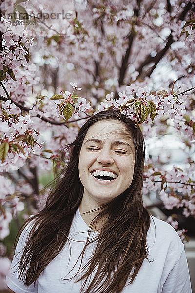 Lächelnde junge Frau steht an rosa Baum