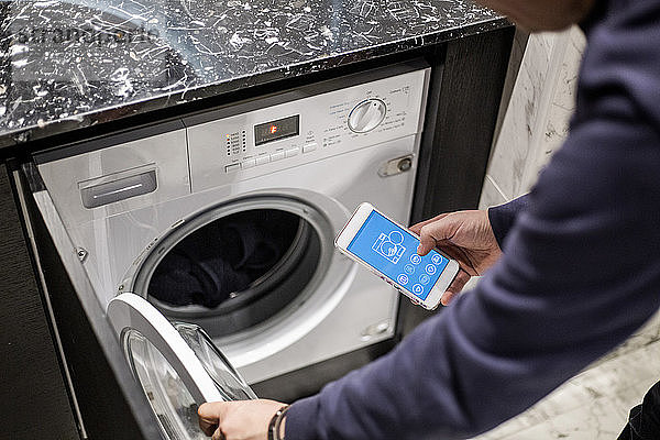 Ausgeschnittenes Bild eines Mannes  der die Waschmaschine mit einer mobilen App im Smart Home steuert