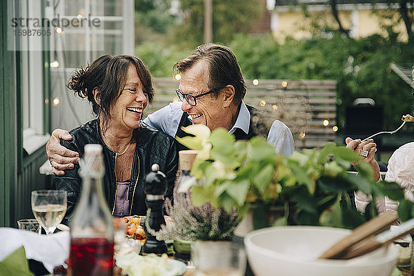 Lächelnder älterer Mann und lächelnde ältere Frau genießen Dinnerparty  während sie im Garten am Esstisch sitzen