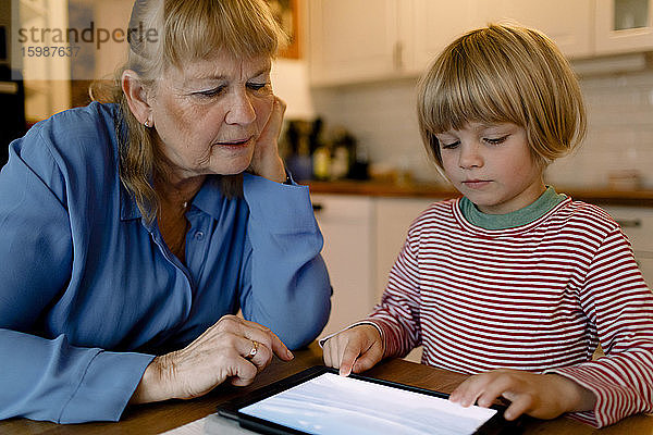 Ältere Frau betrachtet Enkel mit digitalem Tablett