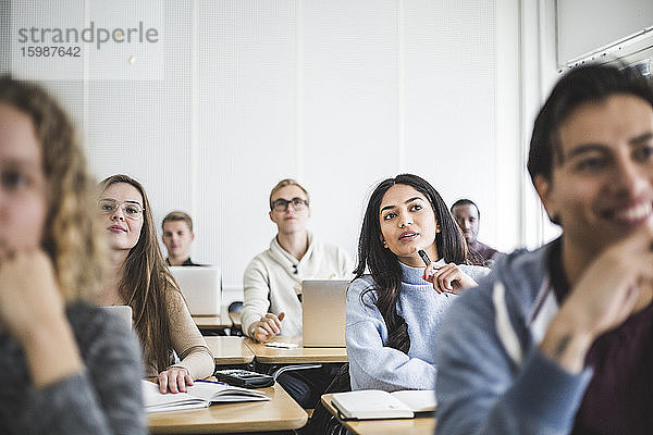 Multi-ethnische männliche und weibliche Studierende  die im Klassenzimmer am Schreibtisch sitzen