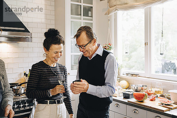 Lächelnder Mann und Frau teilen sich ein Smartphone  während sie in der Küche stehen