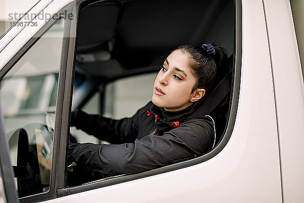 Junge Lieferfrau schaut beim Lkw-Fahren durchs Fenster