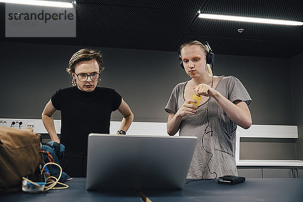 Junge androgyne Kollegen  die im Büro auf den Laptop schauen