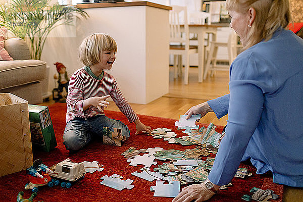 Fröhlicher Junge spielt Puzzle mit Großmutter im Wohnzimmer