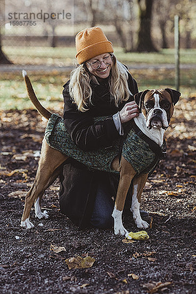 Lächelnde junge Frau betrachtet Boxerhund kniend