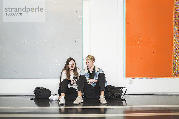 Junger Mann sitzt mit Freundin auf dem Flur der Universität