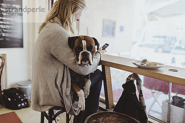 Seitenansicht einer jungen Frau  die ein Smartphone benutzt  während sie mit ihrem Hund im Café sitzt