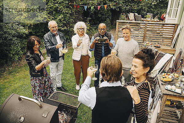 Ältere Männer und Frauen stoßen im Hinterhof auf die Gastgeber der Party an