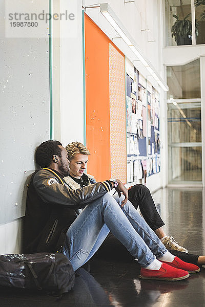 Junger Mann sitzt mit männlichem Freund auf dem Flur der Universität