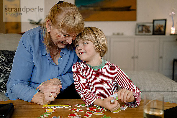 Lächelnder Enkel und Großmutter spielen zu Hause mit dem Puzzle