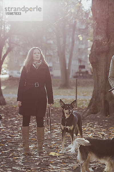 Eine reife Frau in voller Länge schaut weg  während sie mit Hund im Park steht