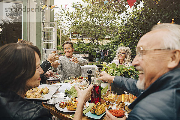 Glückliche ältere männliche und weibliche Freunde genießen die Dinnerparty  während sie am Esstisch im Hinterhof sitzen