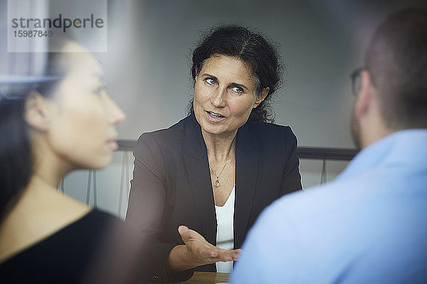Selbstbewusste reife Finanzberaterin diskutiert mit Geschäftsmann und Geschäftsfrau während einer Besprechung im Büro
