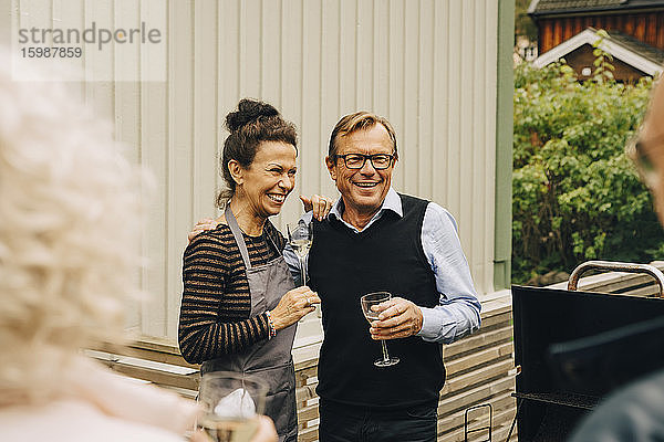 Lächelnder älterer Mann und lächelnde ältere Frau  die während einer Gartenparty im Hinterhof mit dem Arm um den Hals stehen