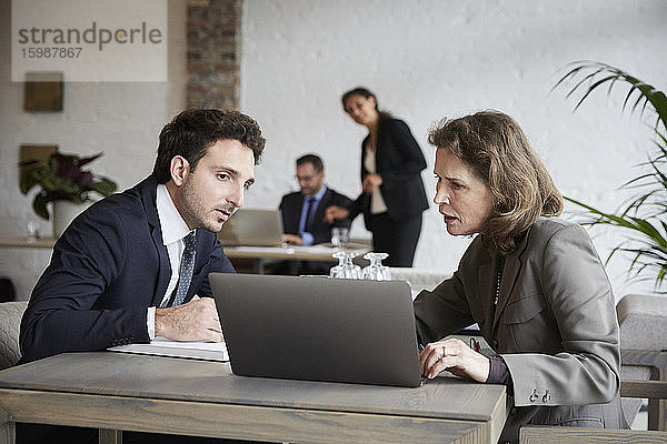 Ältere Anwältin diskutiert mit jungem Geschäftsmann über Laptop während eines Treffens im Büro