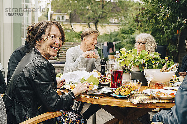 Porträt einer lächelnden älteren Frau  die mit männlichen und weiblichen Freunden am Esstisch sitzt und eine Dinnerparty genießt