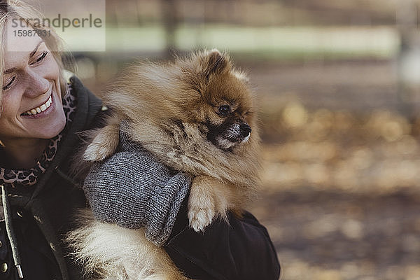 Lächelnde Frau umarmt flauschigen pommerschen Hund im Park