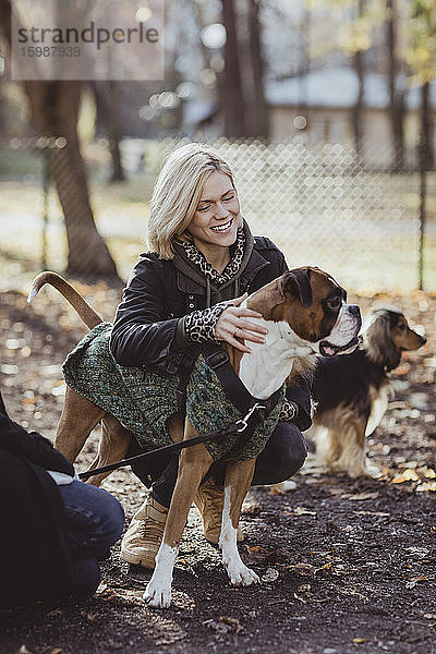 Lächelnde blonde Frau kauert bei Freundin mit Hunden im Park