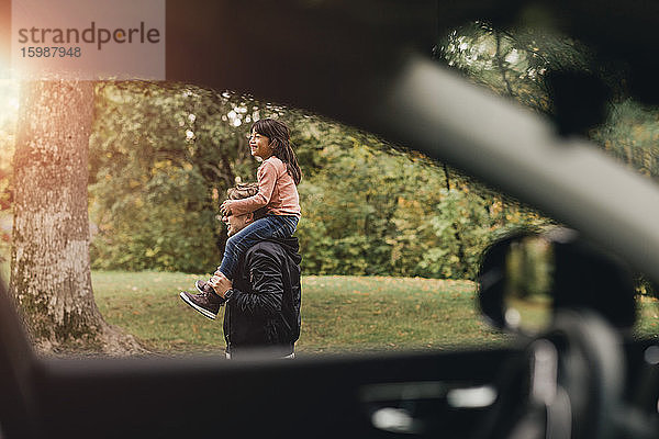 Vater trägt glückliche Tochter beim Picknick am Wochenende auf den Schultern