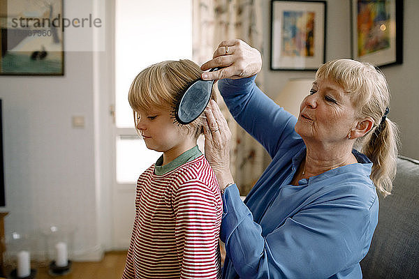 Seitenansicht einer älteren Frau  die zu Hause im Wohnzimmer die Haare ihres Enkels kämmt