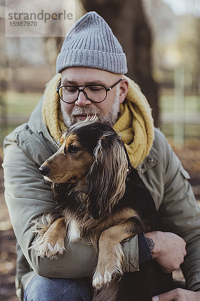 Mann umarmt Hund  während er im Herbst im Park kauert