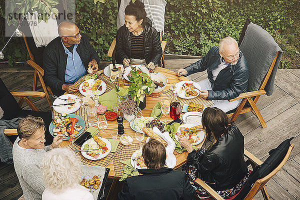 Schrägaufnahme von älteren Freunden  die während einer Gartenparty im Hinterhof am Esstisch essen
