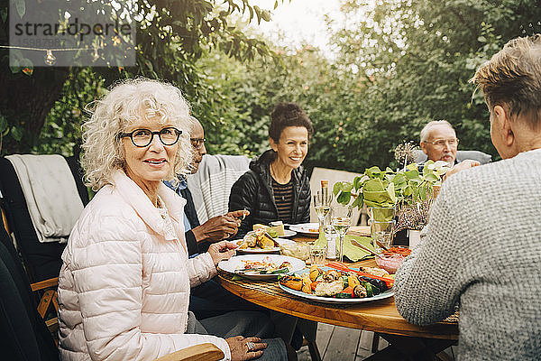 Porträt einer lächelnden älteren Frau  die während der Dinnerparty mit Freunden am Esstisch sitzt