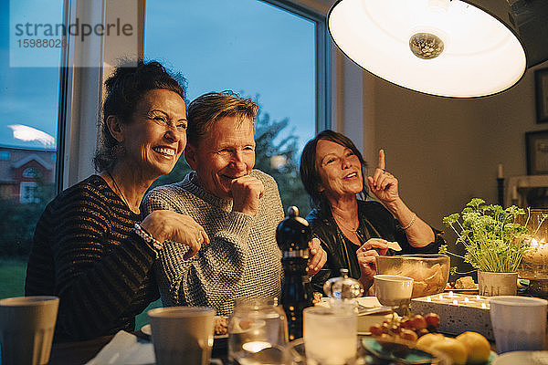Glückliche ältere Frauen und Männer sitzen am beleuchteten Esstisch und genießen die Dinnerparty