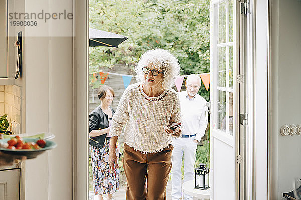 Lächelnde Frau mit lockigem  weißem Haar geht gegen Freunde durch die Tür
