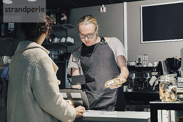 Kunde steht mit transsexueller Kassiererin an der Kasse im beleuchteten Café