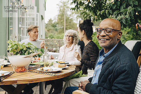 Porträt eines lächelnden kahlköpfigen älteren Mannes  der während der Dinnerparty mit Freunden am Esstisch sitzt