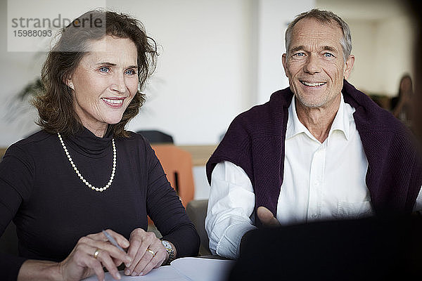Lächelnde ältere Frau sitzt mit einem Mann während eines Treffens in einer Anwaltskanzlei