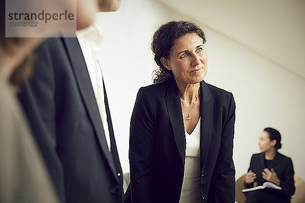 Zuversichtliche Geschäftsfrau schaut weg  während sie während einer Besprechung mit Anwälten im Büro steht