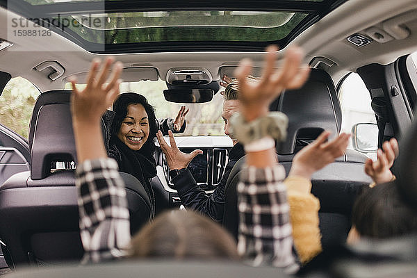 Fröhliche Familie reicht sich die Hand und genießt die Fahrt im Elektroauto