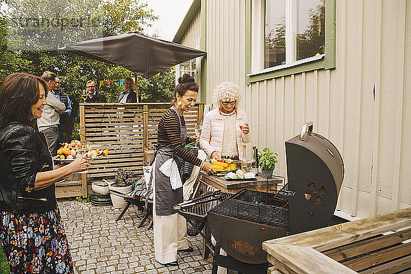 Lächelnde ältere Frauen beim Zubereiten des Abendessens auf dem Grill im Hinterhof