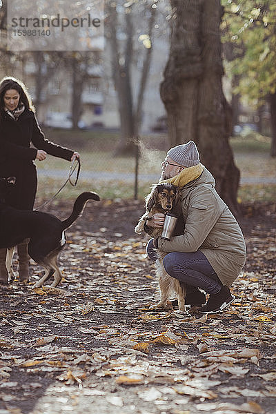 Mann kauert in voller Länge  während er Hund von Frau mit Haustier im Park umarmt