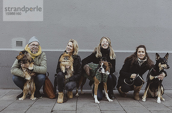 Porträt von lächelnden Haustierbesitzern mit Hunden auf einem Fußweg gegen eine Mauer in der Stadt