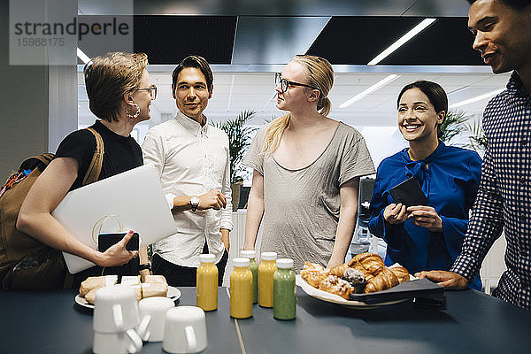 Kollegen diskutieren  während sie bei Essen und Trinken am Tisch im Büro stehen