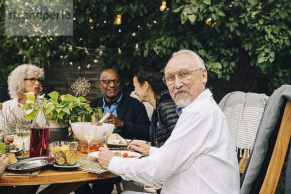 Porträt eines lächelnden älteren Mannes  der mit Freunden bei einem Abendessen am Esstisch sitzt