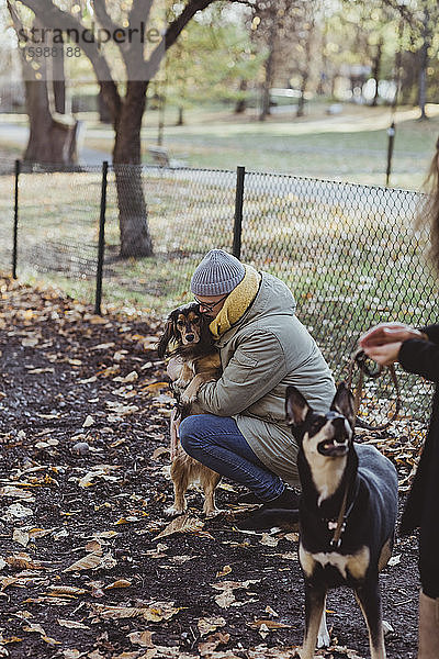 Seitenansicht eines kauernden Mannes  der einen Hund im Park umarmt