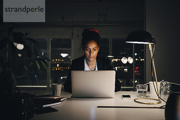 Engagierte junge Geschäftsfrau arbeitet bis spät in die Nacht  während sie den Laptop im Kreativbüro benutzt