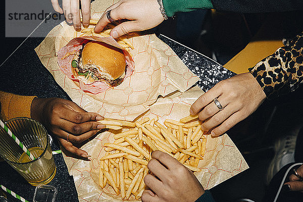 Schrägaufnahme von Freunden  die Burger und Pommes Frites am Tisch im Café essen