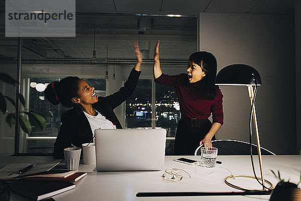 Fröhliche Unternehmerinnen geben High-Five  während sie spät im Amt sind